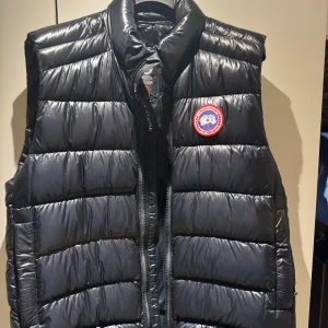 Canada Goose väst - Säljer en svart dunväst från Canada Goose med ett märke på bröstet. Västen har en quiltad design och dragkedja framtill. Köpt på Johnells, som ny.