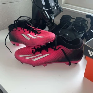 Rosa fotbollsskor Adidas X Speedportal.3 FG - Säljer ett par rosa Adidas X Speedportal.3 FG fotbollsskor med svarta och vita detaljer. Skorna har snörning och är designade för att ge bra grepp på fasta underlag. Perfekta för fotbollsspelare som vill ha både stil och funktion. Säljs i väldigt bra skick, endast använda 1 gång. STÅR INTE FÖR POST SLARV‼️‼️