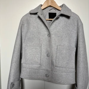 Grå jacka - Snygg grå jacka från Lager 157 i en stilren design. Jackan har en klassisk krage och knäppning framtill med stora knappar. Två praktiska fickor framtill ger extra stil och funktionalitet.