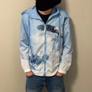 Blå Trapstar - Snygg blå vindjacka från Trapstar med coolt örnmönster. Jackan har dragkedja framtill och en huva för extra skydd. Perfekt för en stilren look med en touch av naturinspiration. Pris kan diskuteras