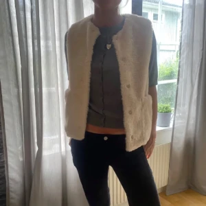 Beige pälsväst - Säljer en mysig beige pälsväst som är perfekt för kyligare dagar. Västen har en enkel design utan knappar eller dragkedja, vilket ger en stilren look. Passar bra över en tröja eller långärmad topp.