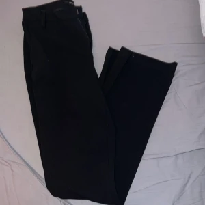 Svarta kostymbyxor från ONLY - Snygga svarta kostymbyxor från ONLY med en stilren design. Byxorna har en dragkedja och knapp framtill samt hällor för bälte. Perfekta för en elegant look. Det är storlek s/32