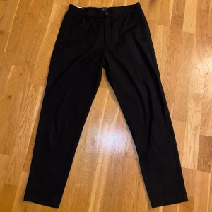 Svarta byxor från Gabba - Snygga svarta byxor från Gabba i en stilren design. Byxorna har en elastisk midja och stängs med knapp och dragkedja. Perfekta för en avslappnad men stilfull look.