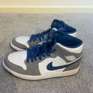 Nike Air Jordans i grått och vitt - Snygga Nike Air Jordans i en stilren kombination av grått och vitt med blå detaljer. Skorna har klassisk snörning och den ikoniska Air Jordan-loggan på sidan. Perfekta för dig som vill ha en sportig och trendig look.pris är förhandlingsbart 