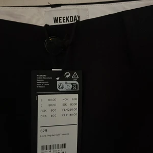 Svarta kostymbyxor från Weekday, taggen kvar  - Oanvända svarta kostymbyxor från Weekday med en klassisk rak passform. Byxorna har en stilren design med knappar bak och är perfekta för en dressad look. Passar bra till både formella och avslappnade tillfällen.