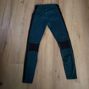 Träningsleggings från Energetics - Snygga träningsleggings från Energetics i en kombination av blått och svart. De har en hög midja och är tillverkade i ett syntetmaterial med DRY-PLUS teknologi för att hålla dig torr under träningen. Perfekta för gymmet eller löprundan.