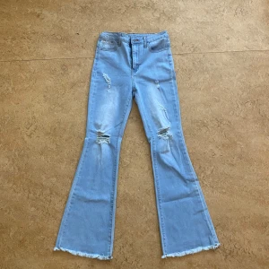 Ljusblå bootcut jeans från Shein - Snygga ljusblå bootcut jeans från Shein med slitna detaljer och fransade benslut. Perfekta för en avslappnad stil med en modern touch. Passar tonåringar i storlek 158.