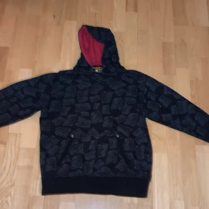 Rare fishbone hoodie - Säljer en svart hoodie från Fishbone med ett unikt mönster i grått. Hoodien har en röd insida i huvan och praktiska fickor framtill. Perfekt för en avslappnad stil.