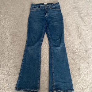 Blå bootcut jeans från Gina - Snygga blå bootcut jeans från Gina med klassisk femficksdesign. De har en dragkedja och knapp framtill. Perfekta för en avslappnad stil med en touch av retro.