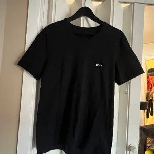Svart t-shirt från Boss - Snygg svart t-shirt från Boss i storlek M. Den har en enkel design med korta ärmar och en liten logotyp på bröstet. Perfekt för en stilren look.