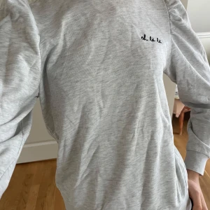 Grå sweatshirt med text - Säljer en stilren grå sweatshirt med texten 'oh la la' broderad på bröstet. Tröjan har långa ärmar och en bekväm passform, perfekt för en avslappnad look. Passar bra till jeans eller leggings.