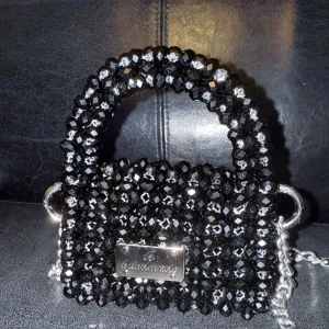 “Black glittery handbag - Snygg svart handväska täckt av glittriga pärlor och en silverfärgad kedja. Perfekt för att ge en extra touch till din outfit. Väskan har en liten metallplatta med texten 'handmade'.
