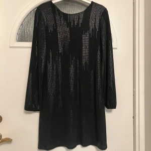 Svart glittrig klänning från SisterS Point - Snygg svart klänning från SisterS Point med glittriga detaljer som ger en festlig look. Klänningen har långa ärmar och en rak passform, perfekt för en kväll ute. Materialet är mjukt och bekvämt.