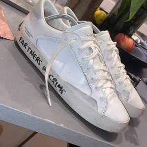 Crime london skor - Snygga vita sneakers med texten 'PARTNERS IN CRIME' på sidan. Skorna har snörning och en klassisk design med en tjock sula. Perfekta för en avslappnad stil. Går ner i pris vid snabb affär