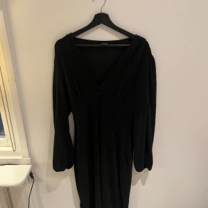 Svart glittrig klänning från Gina tricot  - Snygg svart klänning från Gina tricot  med glittrigt material och v-ringad design. Klänningen har långa ärmar och knappar framtill. Perfekt för en kväll ute eller en speciell tillställning.