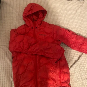 Jacka Peak Performance - Säljer en snygg röd dunjacka från Peak Performance. Jackan har en quiltad design med dragkedja och huva. Perfekt för kyliga dagar och håller dig varm och bekväm. Den har en stilren look med diskret logga på ärmen.  Pris kan diskuteras, även vissa byten kan vara intressant 