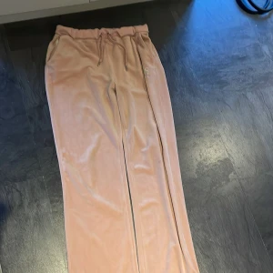 Rosa mjukisbyxor med glitterdetaljer - Snygga rosa mjukisbyxor med glittrande textdetaljer på baksidan. Byxorna har en bekväm passform med resår i midjan och snörning för justering. Perfekta för en avslappnad stil med en touch av glamour.