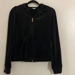 Svart velourjacka med dragkedja - Snygg svart velourjacka med dragkedja och huva. Jackan har långa ärmar och praktiska fickor framtill. Perfekt för en avslappnad stil.