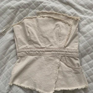 Beige jeans topp - Säljer en beige axelbandslös jeans topp. Toppen har en figurnära passform, perfekt för en stilren look. Använd en gång från Zara.