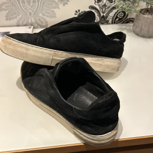 Svarta sneakers i mocka - Snygga svarta sneakers i mocka med en vit sula. Skorna har en stilren design utan snörning, vilket ger dem ett minimalistiskt utseende. Perfekta för en avslappnad stil.