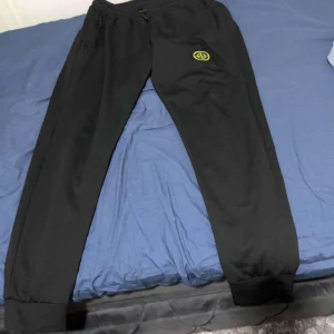 Svarta mjukisbyxor från Stone Island - Säljer ett par svarta mjukisbyxor från Stone Island med elastisk midja och ribbade muddar. Byxorna har den ikoniska logotypen på benet. Perfekta för en avslappnad stil.