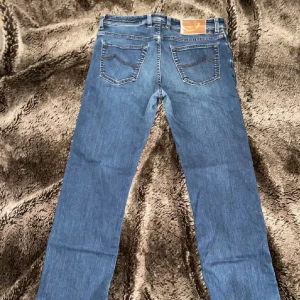 Blå jeansbyxor från Jacob Cohen - Snygga blå jeansbyxor från Jacob Cohen med knappgylf och klassisk femficksdesign. Byxorna har en straight passform och är perfekta för en avslappnad stil. Märket '620 Special' syns på insidan av gylfen. Storlek 32/32 passar perfekt om du är mellan 180-185.