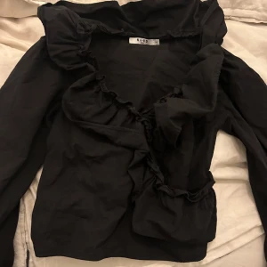 Svart blus från NA-KD - Elegant svart blus från NA-KD med volangdetaljer längs halsringningen och framsidan. 