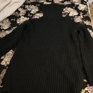 Svart ribbad polotröja 250-150 - Säljer en stilren svart ribbad polotröja med långa ärmar. Perfekt för kyliga dagar och enkel att matcha med olika outfits. Tröjan har en hög krage som håller dig varm och bekväm.