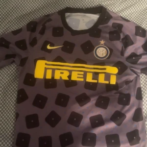 Inter Milan fotbollströja från Nike - Säljer en unik Inter Milan fotbollströja från Nike med ett iögonfallande mönster i svart och lila. Tröjan har korta ärmar och det klassiska Pirelli-trycket på framsidan. Perfekt för samlare eller fans av laget! Den är oxå använd fåtal gånger och priset kan diskuteras :)