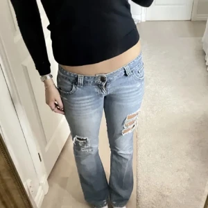 Ljusblå slitna jeans - Snygga ljusblå jeans med slitningar på framsidan och bakfickorna. De har en låg midja och en bootcut-stil som ger en avslappnad look. Perfekta för en trendig vardagsstil.