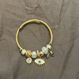 Guldarmband med berlocker - Elegant guldarmband med flera unika berlocker, inklusive en ögonberlock med blå detalj och glittrande stenar. Perfekt för att ge en personlig touch till din stil. Den är från Shein