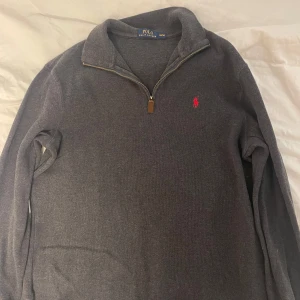 Ralph lauren half zip tröja - Säljer en stilren grå tröja från Ralph Lauren med dragkedja och det klassiska röda logotypbroderiet på bröstet. Perfekt för en avslappnad men snygg look.