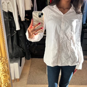 Vit skjorta - Klassisk vit skjorta med krage och knappar framtill. Perfekt för en stilren look. Skjortan har långa ärmar och en avslappnad passform.