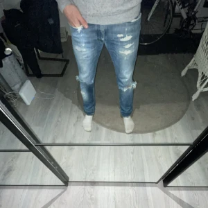 Blå jeans från Reign Italia - Snygga blå jeans från Reign Italia med slitna detaljer och en klassisk femficksdesign. Perfekta för en avslappnad stil. Märkespatch i läder baktill ger en extra touch. Storlek 30 hör av er vid frågor o funderingar
