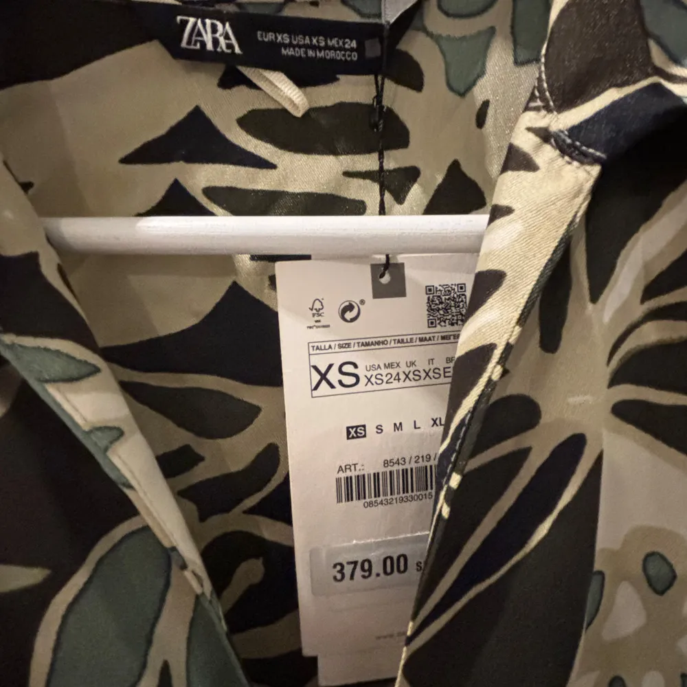 Snygg blus från Zara med ett unikt mönster i grönt, svart och beige. Blusen har långa ärmar och en klassisk krage. Perfekt för att ge din outfit en trendig touch.. Paidat.