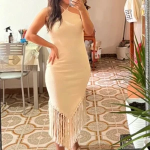 Beige  klänning med fransar - Fin beige klänning med en kytning runt halsen och fransdetaljer längst ner. Endast använd en gång.