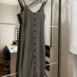 Grå ribbad klänning med knappar - Snygg grå ribbad klänning med smala axelband och knappar framtill. Perfekt för en avslappnad stil.
