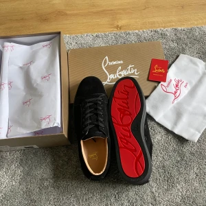 Svarta sneakers från Christian Louboutin - Snygga svarta sneakers från Christian Louboutin med den ikoniska röda sulan. Skorna har snörning och är tillverkade i mocka, vilket ger en lyxig känsla. Perfekta för den stilmedvetna som vill ha något extra i garderoben. Helt nya skor aldrig använda 10/10 skick. Alla tillbehör medföljer 