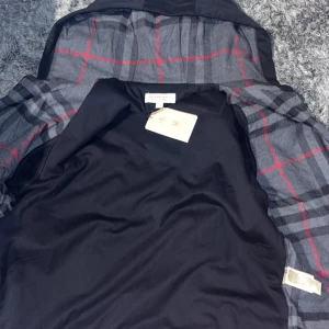 Svart jacka från Burberry - Snygg svart jacka från Burberry med klassiskt rutigt foder i grått och rött. Perfekt för en stilren look. Jackan har en elegant design och är tillverkad i högkvalitativt material.