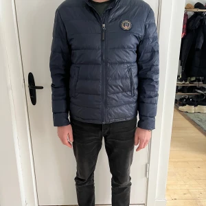 Mörkblå jacka från Lexington (man) - Säljer en marinblå Lexington jacka i storlek L. Jackan har en lättviktig design med quiltade paneler och dragkedja framtill. Tillverkad i slitstarka material med broderad Lexington-logga på bröstet. Passar perfekt för en vardagslook under höst- och vintermånaderna.  Personen på bilderna är 184 cm lång.  Skick: Mycket gott skick med små tecken på användning.  Nypris: 2 000 SEK
