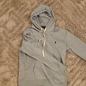 Grå polo hoodie - Säljer min grå hoodie från Ralph Lauren med klassisk logga på bröstet. Fodrad inuti och har knappt använt den