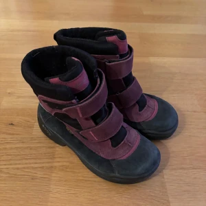 Svarta och lila Gore-Tex boots från Ecco - Säljer ett par svarta och lila boots från Ecco med Gore-Tex teknologi. Skorna har praktiska kardborreband och en robust sula för bra grepp. Perfekta för kyligare väder eller regn! 