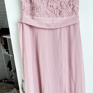 Rosa spetsklänning med slits - • Lång, lyxig och elegant klänning.  • Använd enbart vid ett tillfälle.  • Öppen rygg.  • Spets framtill och bak.  • Skärp finns till klänningen • Slits finns snett framtill.  • Såg nu att det fanns 2 små fläckar som syns i Vissa ljus och ändå Mycket Otydligt. (Se bild 6). Fick kämpa med att lyckas fånga de på bild då fläcken syns mycket otydligt.