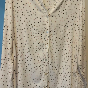 Vit prickig blus från Kaffe - Säljer en söt vit blus från Kaffe med små prickar i svart och rosa. Blusen har långa ärmar och knappar framtill. Perfekt för en stilren och lekfull look.