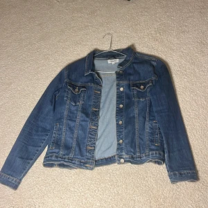 Blå jeansjacka från Deal - Snygg blå jeansjacka från Deal i storlek XL. Jackan har klassisk design med knappar framtill och två bröstfickor med knappstängning. Perfekt för en avslappnad stil. Står XL men passar som S