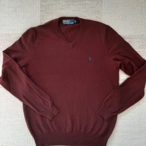 Vinröd tröja från Polo Ralph Lauren - Säljer en stilren vinröd tröja från Polo Ralph Lauren i 100% merinoull. Tröjan har en v-ringad design och ett diskret broderat logotypmärke på bröstet. Perfekt för kyligare dagar. Ny pris 2395 kr. Kontakta om ni undrar över något!