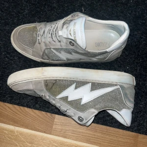 Zadig & Voltaire sneakers - Snygga grå sneakers med en vit blixtdetalj på sidan. Skorna har snörning med text på skosnörena och en vit sula. Perfekta för en avslappnad stil. Rengörs innan jag postar såklart!!!!! Köpt för 4000. Pris kan diskuteras