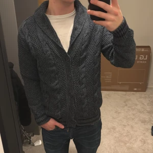 Mörkblå stickad kofta från Coogi - Säljer en snygg mörkblå stickad kofta från Colins med kabelstickat mönster. Koftan har en djup v-ringning och knappar framtill. Perfekt för kyliga dagar! Nypris på denna är 1500kr. Den är i nyskick. Skriv vid funderingar!🥂🥂