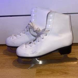 Vita konståkningsskridskor - Säljer ett par vita konståkningsskridskor från Safine. De har snörning och en klassisk design med robusta blad för isdans eller träning. Perfekta för vintersäsongen!