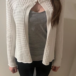 Vit ribbad kofta - Säljer en stilren vit ribbad kofta med långärmad design. Koftan har en enkel knäppning framtill och ett våfflat mönster som ger en unik textur. Perfekt för lager-på-lager-stil. Helt oanvänd och så fin bara lite liten på mig😇 (inte jag på bilden)